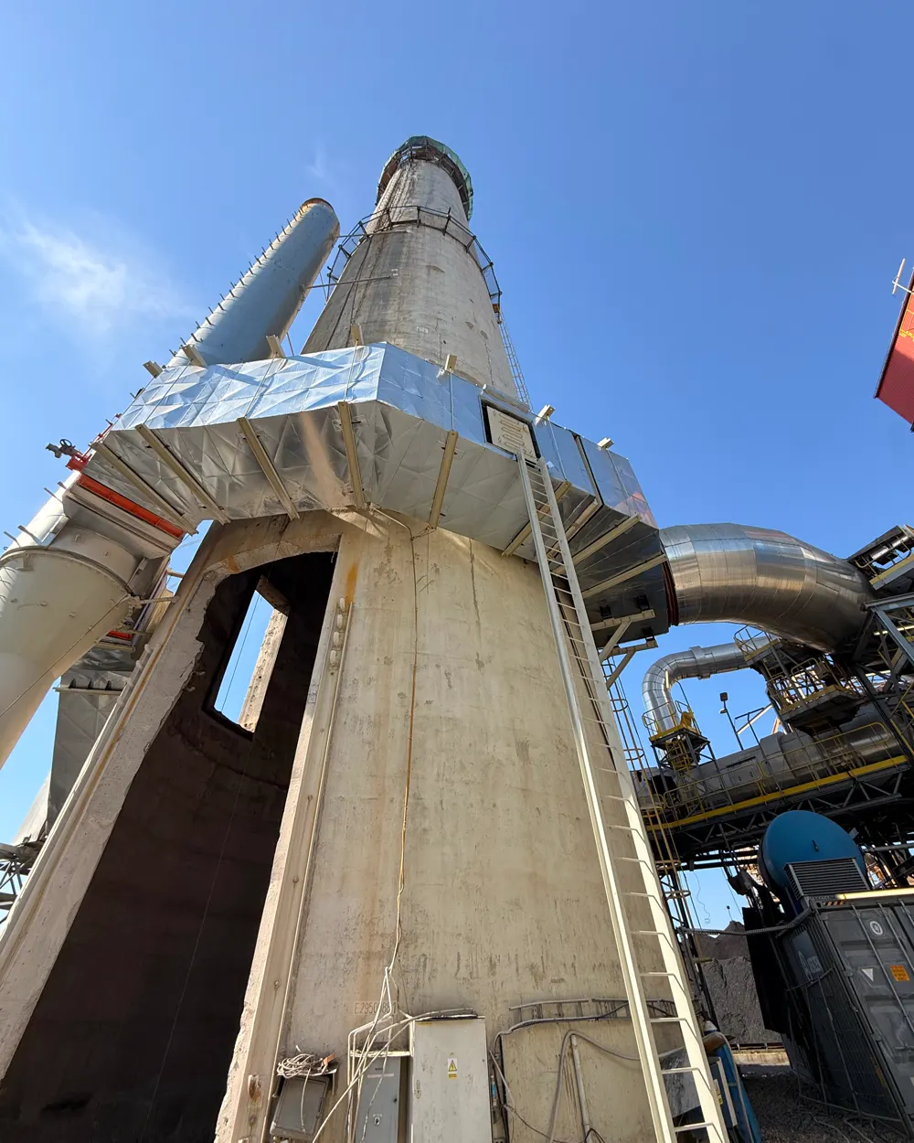 Żelbetowy komin przemysłowy z platformą roboczą i prostokątnym otworem technologicznym wyciętym techniką diamentową