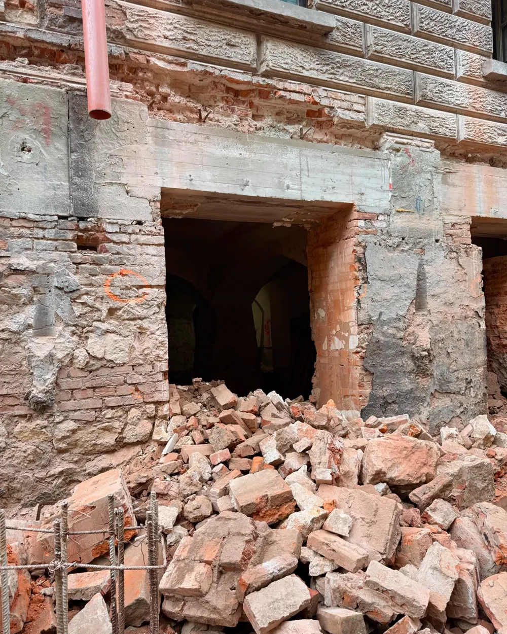Prostokątny otwór wycięty w ceglanym murze fundamentowym, w głębi sklepienie piwnicy, przed otworem pryzma gruzu ceglanego