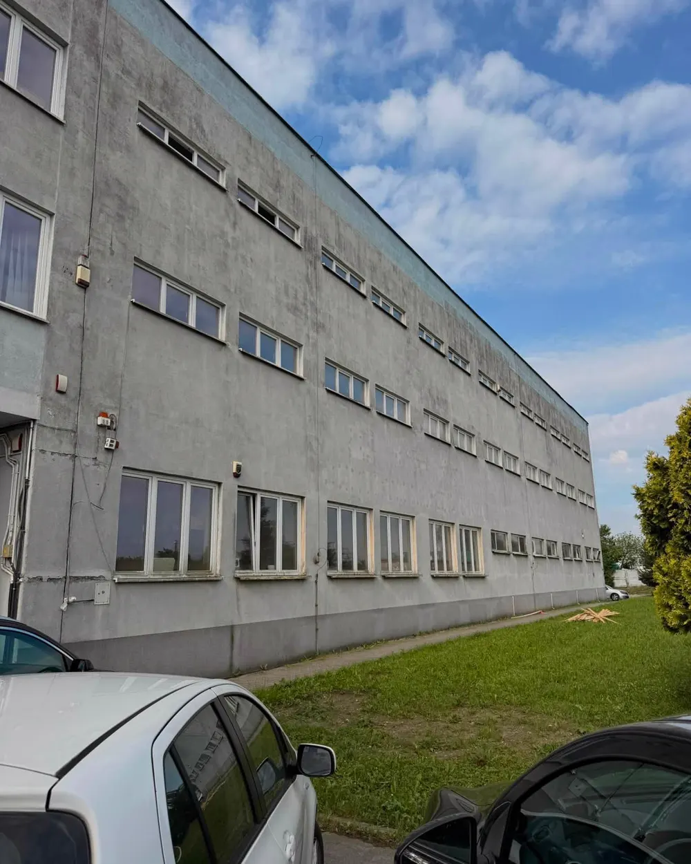 Elewacja trzykondygnacyjnego budynku przemysłowo-biurowego przed pracami — wąskie pasmowe okna w betonowej ścianie