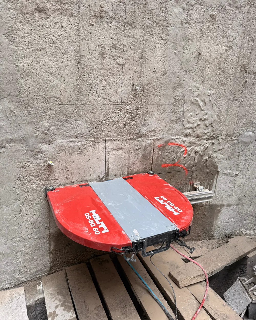 Detal czerwonej głowicy piły ściennej Hilti zamontowanej na szynie obok świeżego cięcia w żelbetowej ścianie